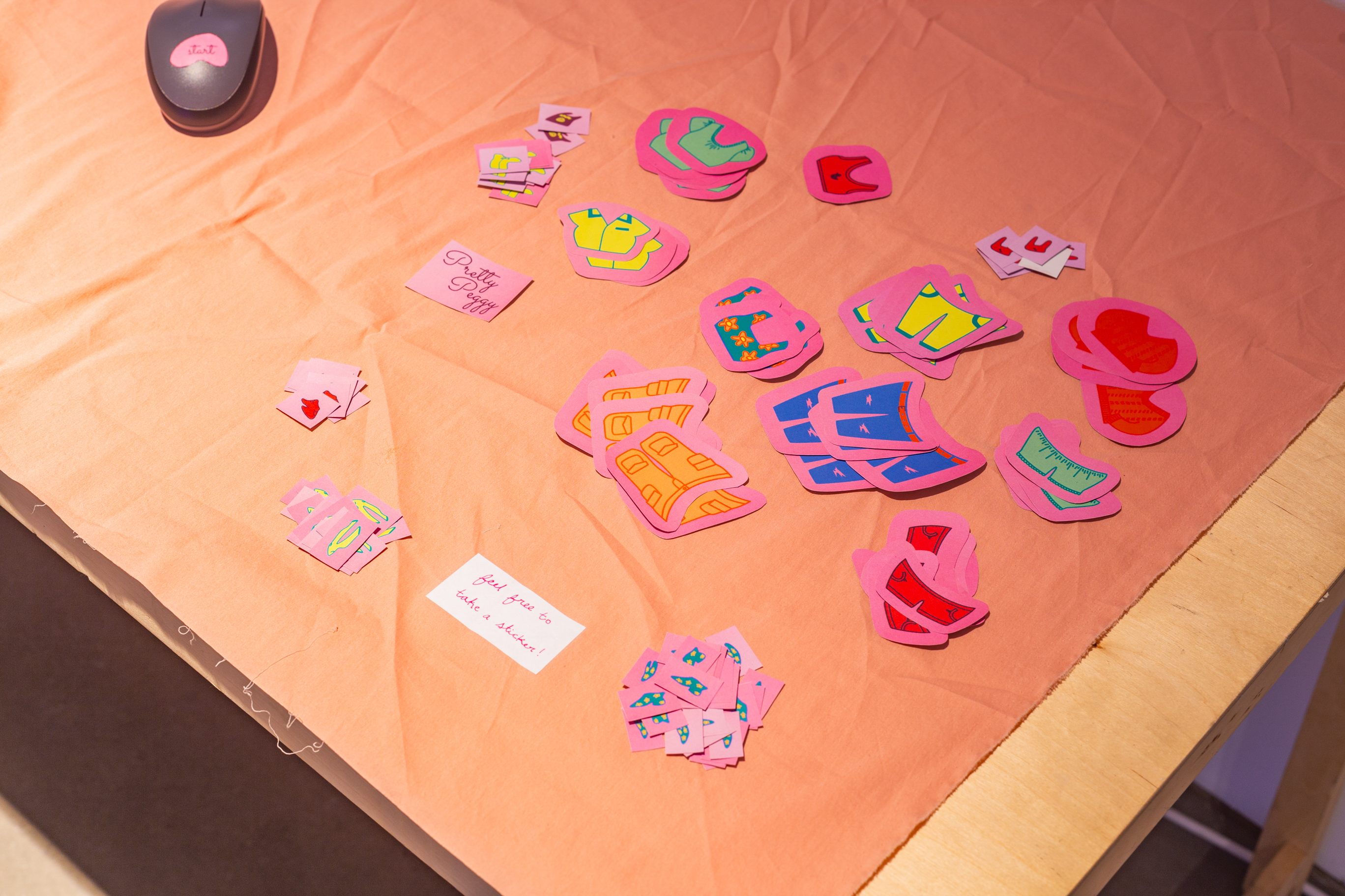 Stickers of various items created by the artist is displayed on the table, with a note that reads Feel Free to take one.